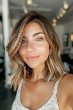 Smiling woman with shoulder-length, wavy hair standing in a well-lit room. Partial Highlights Light Brown Hair, Light Brown Lob With Highlights, Root Melt Brunette To Blonde Short Hair, Dark Blonde Balayage Short, Soft Brown Hair With Highlights, Highlights On Light Brown Hair, Short Brunette Hair With Highlights, Short Dark Blonde Hair, Blonde Ombre Short Hair