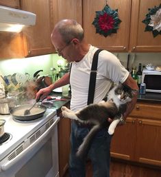 a man holding a cat in his arms while standing next to a stove top oven