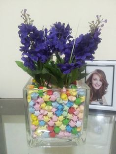 a vase filled with candy stars and purple flowers on top of a table next to a framed photo