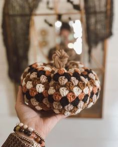 a hand holding a crocheted pumpkin in front of a mirror