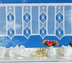 a white crochet curtain hanging over a window next to vases and flowers