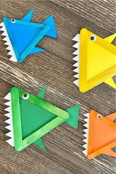 four paper fish on a wooden table with one in the shape of a triangle and another shaped like a shark