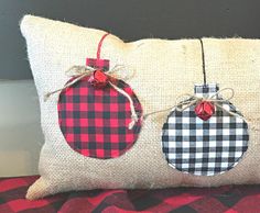 two christmas ornaments are hanging from the back of a burlocked pillow on a red and black checkered blanket