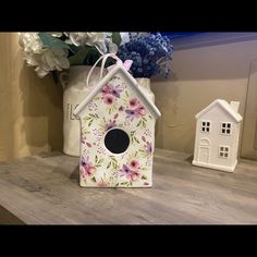 a birdhouse with flowers painted on it sitting on a table next to a vase