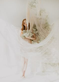 a woman standing in front of a white curtain with flowers hanging from it's sides