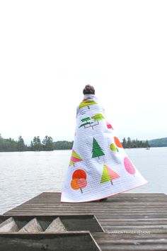 a person sitting on a dock with a blanket over their head, looking out at the water