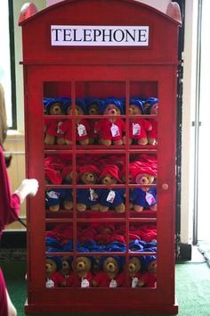 a red phone booth with teddy bears in it's display case, and a person walking by