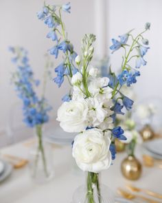 a vase filled with white and blue flowers on top of a table next to gold place settings