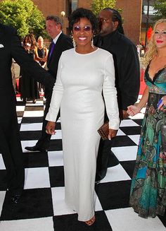 a woman in a long white dress walking down a black and white checkered floor