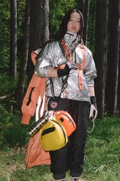 a woman in an orange and silver outfit holding a yellow backpack while standing next to trees