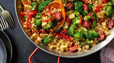 a pan filled with rice, broccoli and other vegetables next to a wooden spoon