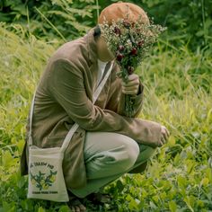 a woman kneeling down in the grass holding a bunch of flowers and looking at her face