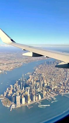 the wing of an airplane flying over a large city and ocean with tall buildings on both sides