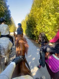 three people riding horses down a dirt road next to trees and bushes on both sides