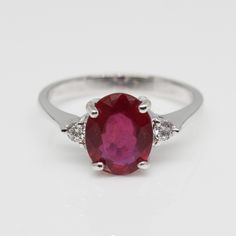 an oval shaped ruby and diamond ring with three diamonds on the sides, set in white gold