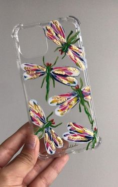 a hand holding up a clear phone case with colorful dragonflies on it