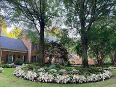 a circular flower bed in front of a brick house with trees and bushes around it