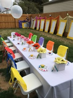 a long table set up for a party with balloons in the air and decorations on it