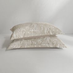 two pillows sitting next to each other on top of a white bed sheet covered in floral print