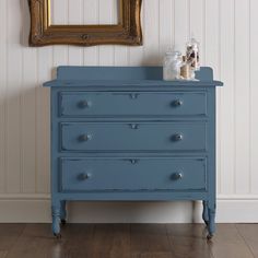 a blue dresser sitting in front of a painting on the wall next to a mirror