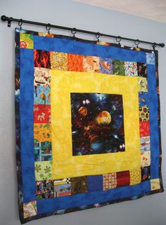 a quilt hanging on the wall in front of a window with an image of planets and stars