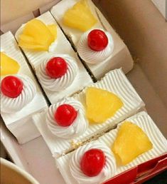 several pieces of cake with pineapples and cherries on top in a box