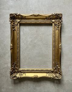 an ornate gold frame hanging on the wall in front of a cement wall with a white background