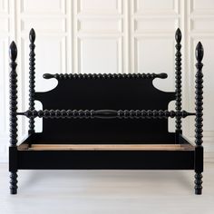 a black bed frame with wooden slats on the top and bottom, in front of a white wall