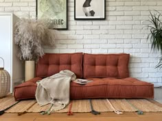 a red couch sitting on top of a wooden floor next to a white brick wall