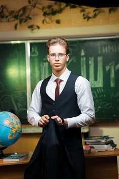 a man wearing glasses and a tie standing in front of a chalkboard