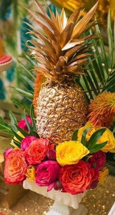 a pineapple and flowers arrangement in a vase on a table with gold sequins