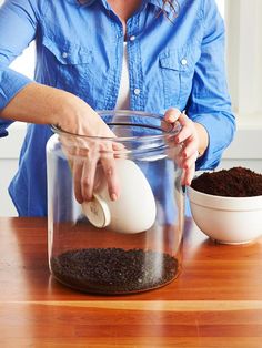 a woman pouring coffee into a glass jar with dirt in the bowl next to it