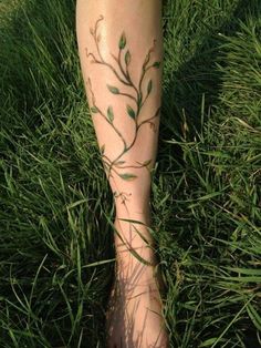 a woman's foot with green leaves on it and grass in the foreground