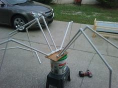 a spider sculpture made out of cans on the sidewalk next to a bench and car