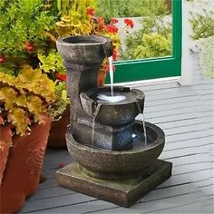 a water fountain sitting on top of a wooden deck next to potted plants