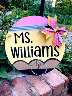 a yellow and pink sign sitting on top of a brick wall next to some flowers