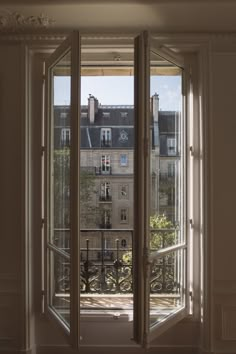 an open door leading to a balcony with buildings in the backgrouds and trees outside