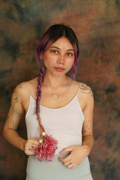 a woman with purple hair wearing a white tank top and holding a flower in her hand