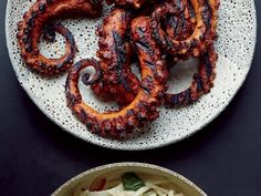 an octopus is served on a plate next to a bowl of noodles and sauces