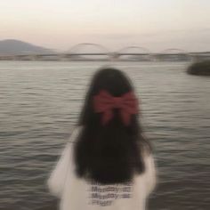 a woman standing in front of the water with a red bow on her head and long black hair