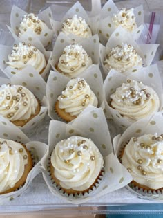 cupcakes with white frosting and gold sprinkles are arranged in paper wrappers