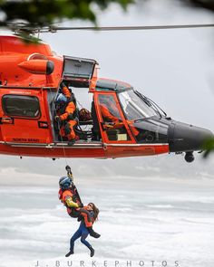 two rescue workers are hanging from the side of a helicopter as another person jumps into the water