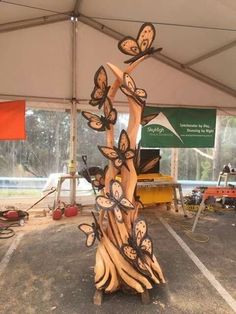 a sculpture made out of wood with butterflies on it in a parking lot under a tent