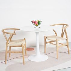 a white table with two chairs and a vase on it's centerpiece in front of a white wall