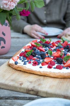 a person sitting at a wooden table with a pizza covered in berries and blueberries