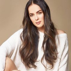 a woman with long brown hair and white sweater sitting on a chair looking at the camera