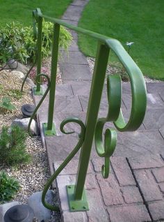 a green metal hand rail sitting on top of a brick walkway next to a lush green lawn