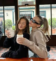 two women sitting at a table drinking coffee and kissing each other with their eyes closed