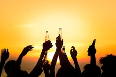 several people raising their hands in the air with beer bottles on top of them at sunset