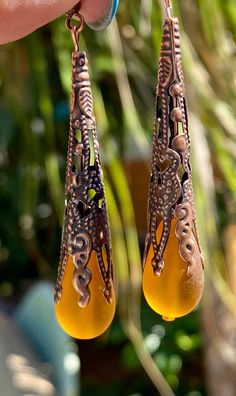 "Dark Amber sea glass glows so pretty in the light. This teardrop is 16x10mm and has an Antique Copper filigree bead cap. They are on solid copper Ear Wires and dangle 2\".  So pretty for this fall or anytime of year. The dark amber with the unique cap is very eye catching  These are made with recycled cultured glass and processed to simulate the effect of mother nature by the sea." Earrings Outfit, Sea Glass Earrings, Fantasy Jewelry, Glass Earrings, Bead Caps, Antique Copper